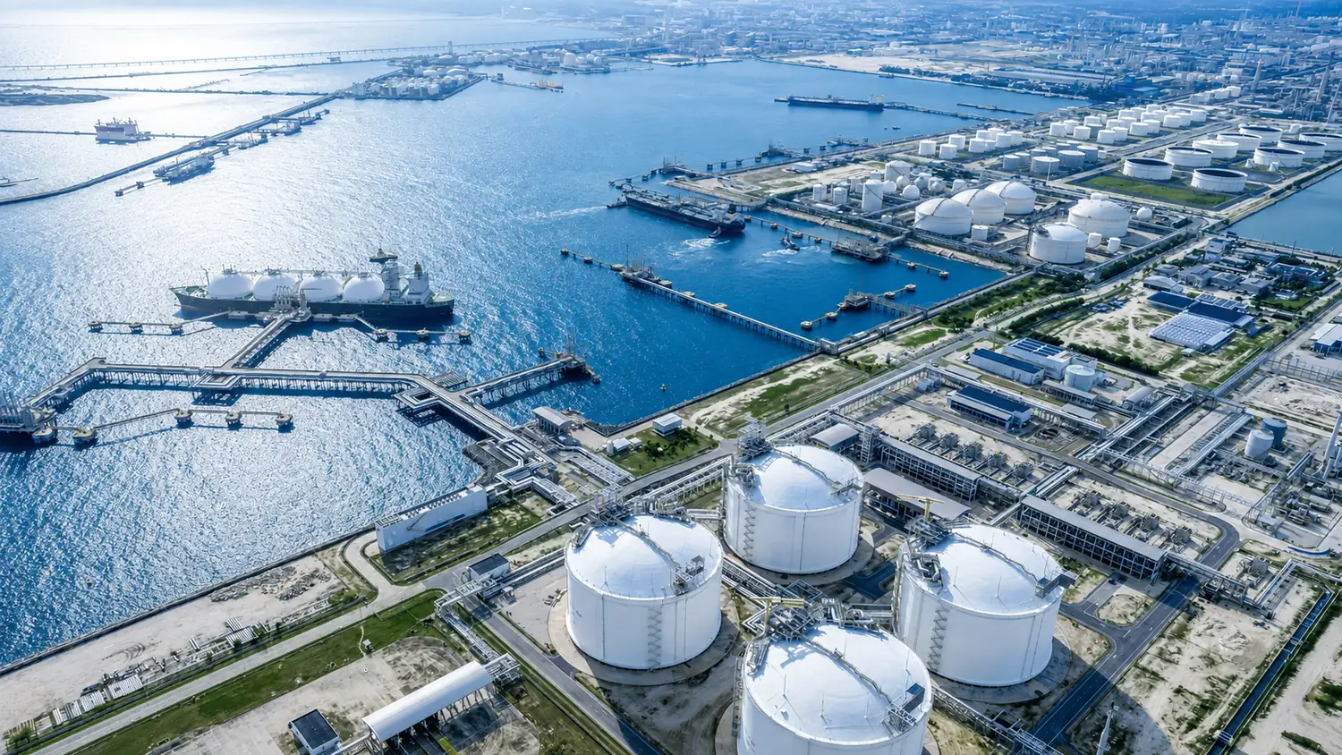 Aerial view of a coastal LNG and oil terminal, its tank farms, jetties and a moored gas carrier